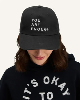 Model wearing black canvas cap embroidered with 'You Are Enough' in white text