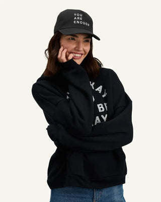 Woman smiling wearing a black We Are Enough canvas cap with motivational text embroidery