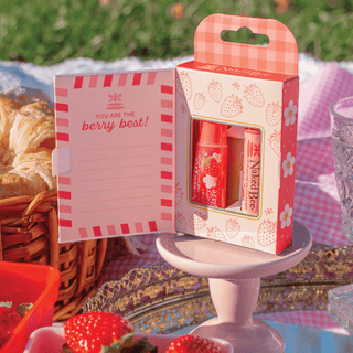 Naked Bee Strawberry Lip Care Duo in pink packaging displayed at a picnic setting