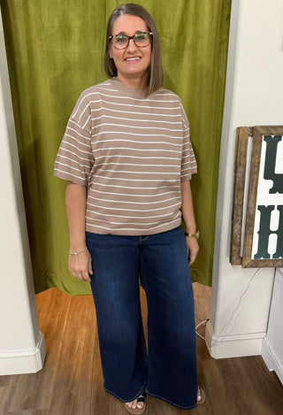 Beige and white striped knit top with ribbed crew neck against olive backdrop