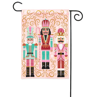 Garden flag featuring three decorative nutcracker soldiers on pink background with gold scrollwork