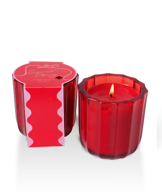 Aromatique Sugared Cherry ribbed red glass candle lit beside its decorative red packaging box