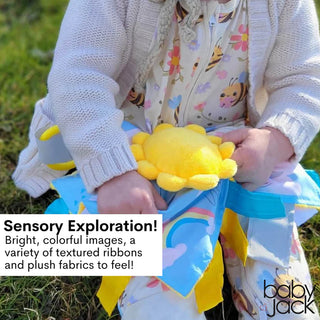 Outdoor close-up of baby grasping textured ribbons on yellow sun lovey