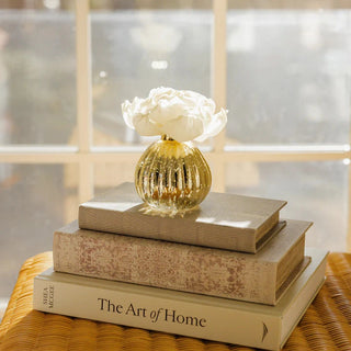 Decorative golden diffuser vase on woven rattan surface with curated home decor books