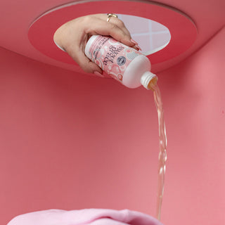 Sweet Grace laundry detergent being poured from bottle onto pink fabric clothing item.