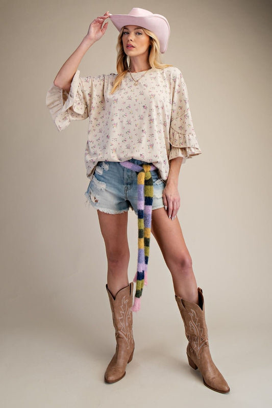 Woman wearing a patterned tan top, denim shorts, and cowboy boots with a colorful scarf.