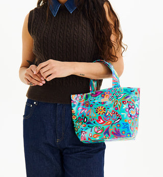 Model holding Consuela Grab N Go Mini tote bag in colorful Tasha print on turquoise background
