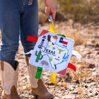 Person holding Texas map crinkle toy with cactus armadillo icons and matte fabric finish