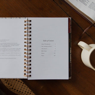 Abide Study Journal open to table of contents, spiral-bound, beside white mug