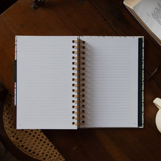 Open spiral-bound lined journal with gold coil binding on a wooden table