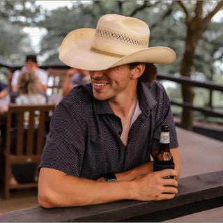 Man wearing a cowboy hat and holding a beer at an outdoor setting