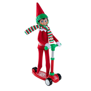 Elf on the Shelf doll in red suit riding a red and green toy scooter with striped scarf