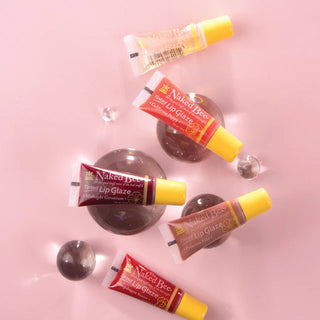 Five-color variety pack of The Naked Bee tinted lip glazes on pink background