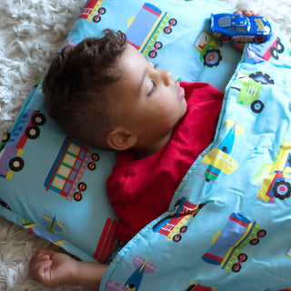Toddler sleeping on blue vehicle print nap mat with built-in pillow and comforter blanket