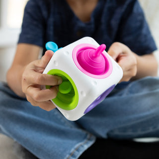 Child holding white Tugl Cube sensory fidget toy with colorful pink, green, blue, and purple silicone spinners