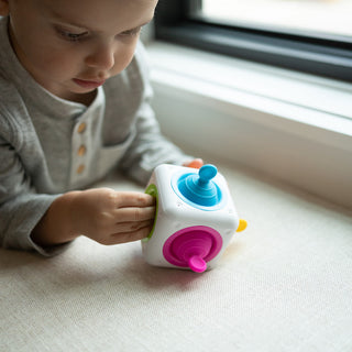 Toddler playing with Fat Brain Toys Tugl Cube featuring colorful spinning and pulling sensory elements