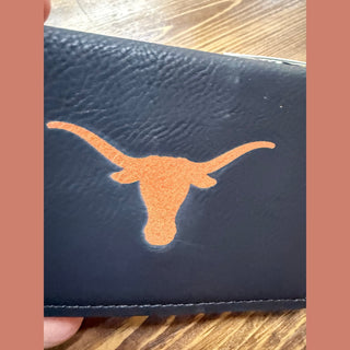 Close-up of pebbled navy leather texture and embossed burnt orange UT Longhorn head logo