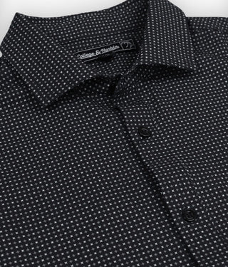 Close-up of a black patterned shirt with a collar and buttons, featuring a brand label.