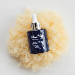 The Naked Bee Vitamin C Renew Face and Neck Serum in dark navy dropper bottle on natural sea sponge
