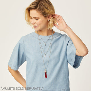 Layered silver charm necklace on model with red tassel and heart pendant for everyday wear