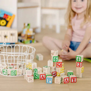 Melissa & Doug wooden ABC blocks scattered on floor with child playing, showing natural wood grain and colorful painted letters numbers