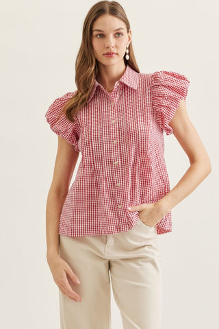 Woman wearing a red and white checkered blouse with ruffled sleeves on a plain background