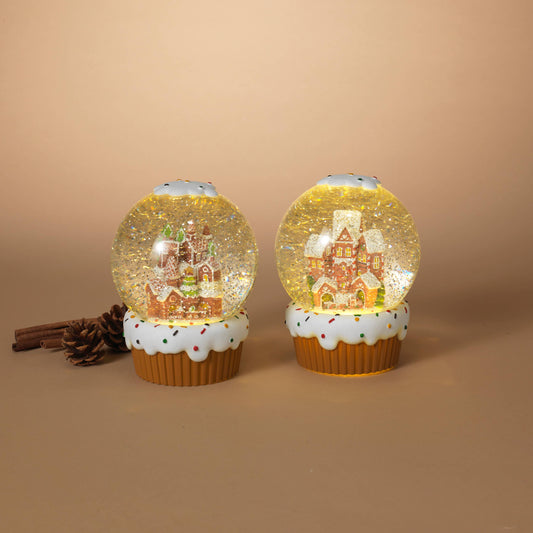Two cupcake-shaped snow globes with gingerbread house designs