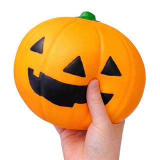 Hand squeezing a large orange jack-o-lantern squishy toy with smiling face