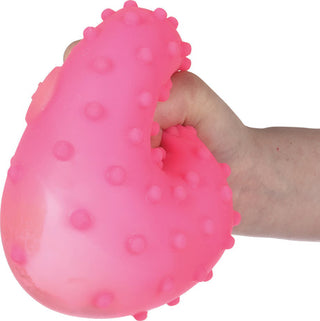 Hand squeezing bright pink textured stress ball with raised bumps on white background