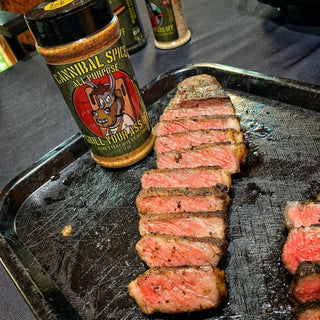 Sliced medium-rare steak with grill marks and seasoning flecks next to GYAO Cannibal all purpose spice shaker on dark metal tray