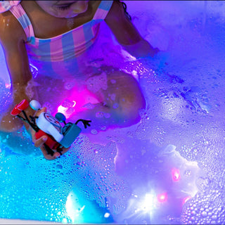 Child playing with glowing red water-activated bath toy cube in bubbly bathtub