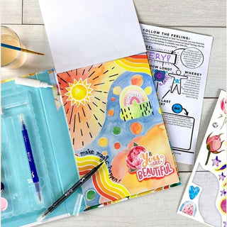 Open Collage Visions Art Journal showing colorful watercolor sunburst spread with included markers and guided activity worksheet