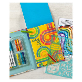 Open art journal with rainbow layered oil pastel and marker artwork on yellow paper, featuring teal geometric stencils and six colorful markers