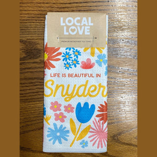 White microfiber tea towel with retro floral pattern and 'Life is Beautiful in Snyder' text, featuring kraft paper tag