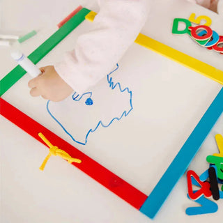 Child drawing blue animal outline on Melissa & Doug white dry-erase board surface with thick wooden frame and scattered magnetic letters