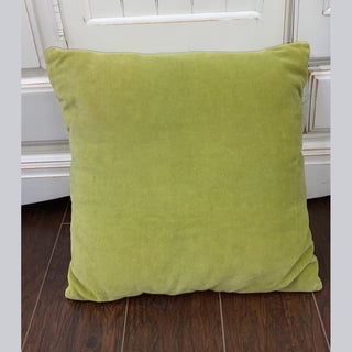 Olive green velvet square pillow with plush texture on dark wood floor