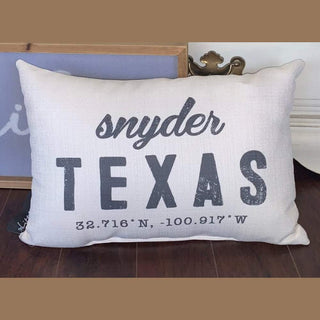 Off-white linen-texture pillow with Snyder Texas coordinates print leaning against brass furniture