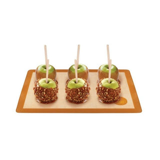 Orange-brown silicone baking mat with textured beige surface holding caramel apples for no-grease food release