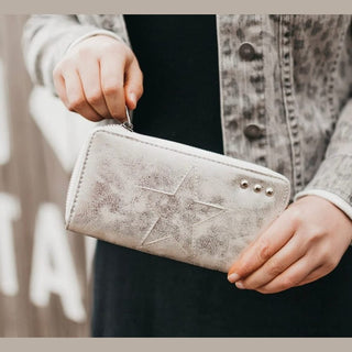 Silver distressed faux leather star wallet held by hand with gray patterned jacket