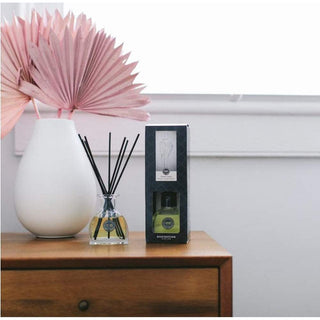Unboxed Sweet Grace Reed Diffuser on wooden dresser with pink dried palm fronds for home fragrance
